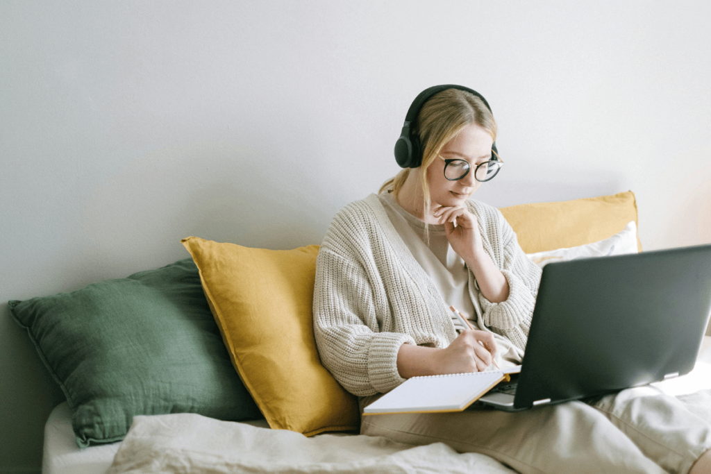 Woman with headphones sitting on a bed and using a laptop